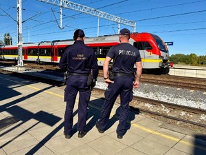 Policjant wraz z funkcjonariuszem służby ochrony koleji obserwują dworzec kolejowy.