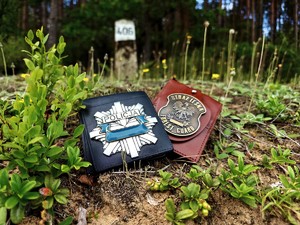 Legitymacje służbowe leżą na leśnej ściółce.