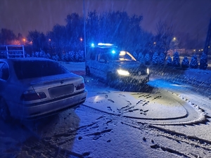 Policyjny radiowóz na sygnałach świetlnych podczas opadów śniegu.