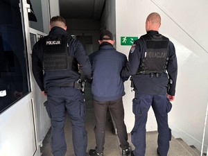 Policjanci trzymają pod rękę poszukiwanego.