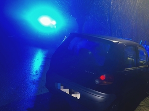 Pojazd zaparkowany na poboczu, w tle widać światła radiowozu.