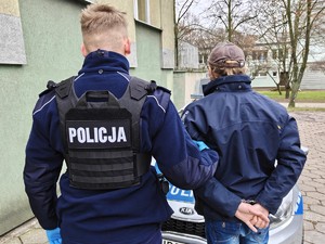 Policjant trzyma pod rękę poszukiwanego.