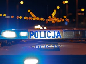 Napis Policja. w tle widoczne odbijające się światła.