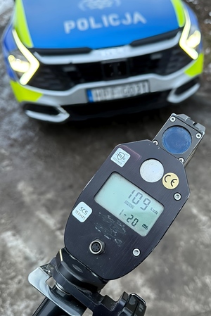 Na mierniku prędkości wyświetla się 109 kilometrów na godzinę. W tle widać policyjny samochód.