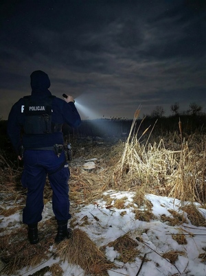 Policjant oświetla sobie drogę latarką.
