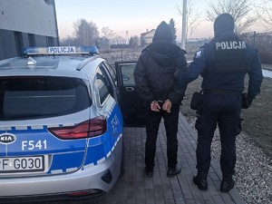 Policjant trzyma pod rękę poszukiwanego mężczyznę.