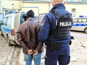 Policjant trzyma pod rękę poszukiwanego mężczyznę.