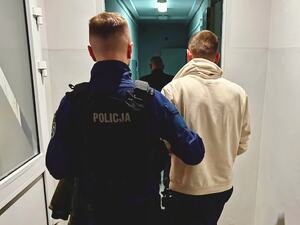 Policjant trzyma pod rękę zatrzymanego.