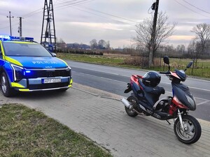 Za motorowerem stoi policyny samochód.