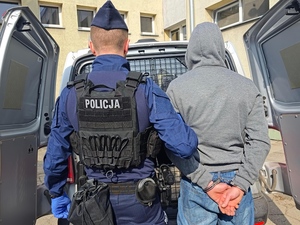 Policjant trzyma pod rękę zatrzymanego.