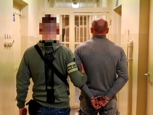 Policjant trzyma pod rękę zatrzymanego.