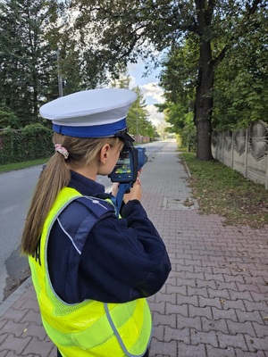 Policjanta z miernikiem prędkości w rękach skierowanym na pojazd.