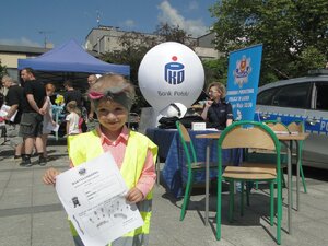 Dziewczynka pozuje do zdjęcia, w rękach trzyma kartkę ze swoimi odciskami palców.
